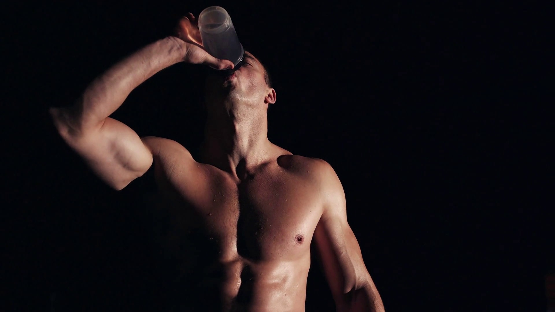 Bình Lắc Nhựa MADI Chính Hãng (700ml) - fit muscular man drinking water or energy drink as he takes a break from working out in a darkened gym close up chest and head showing his strong physique looking into camera rwg emxkqg thumbnail full05